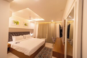 A hotel room with a large bed, a desk, a chair, a television, and a ceiling fan.