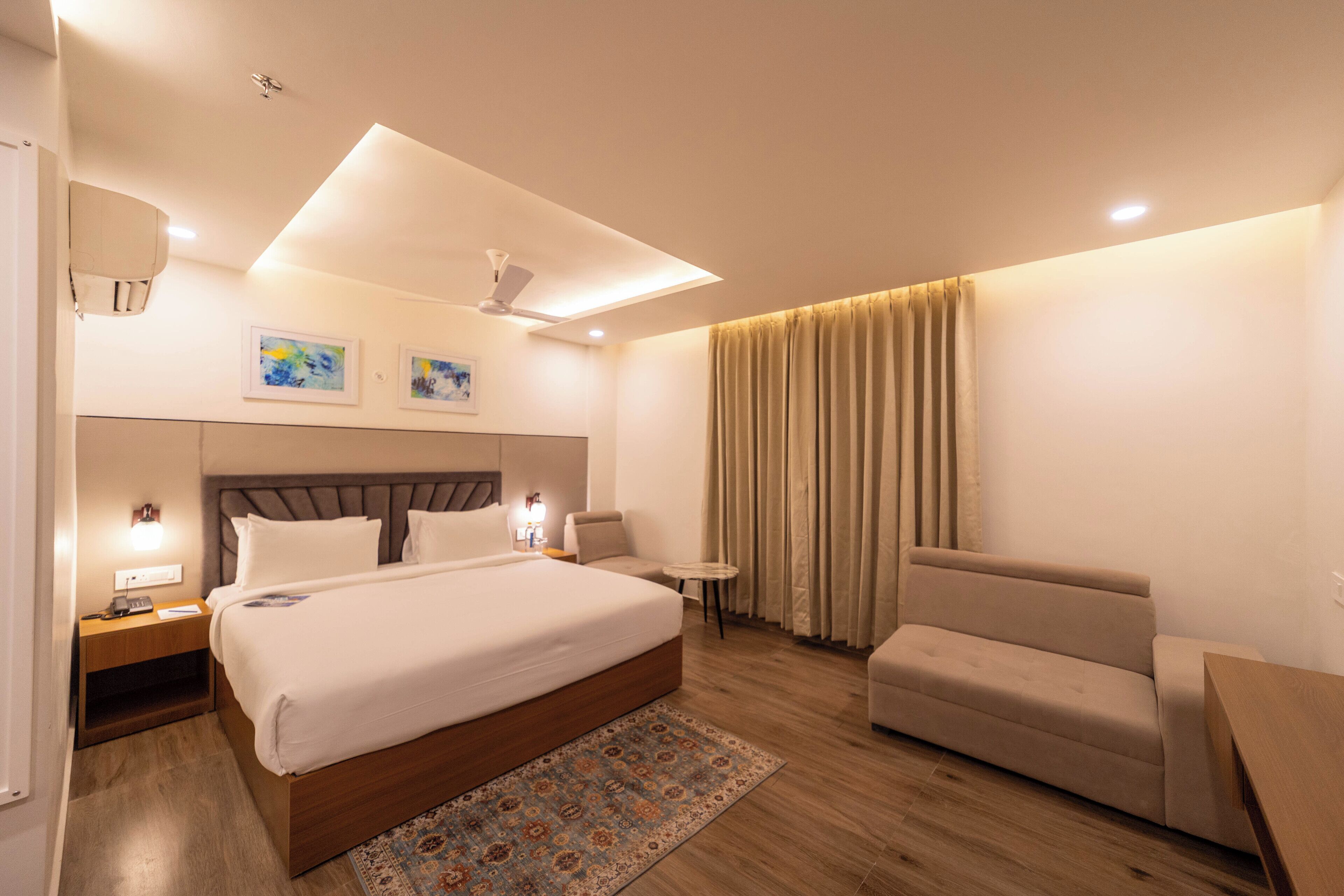 A hotel room with a large bed, a sofa, a small table, and a ceiling fan.
