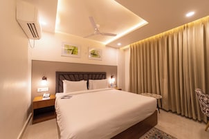 Una habitación de hotel con una cama grande, un ventilador de techo, una mesita de noche con lámpara y una ventana con cortinas.