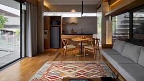A modern living room with a sofa, a coffee table, and a dining area with chairs and a table. - Villa Tana Takah (Bali)