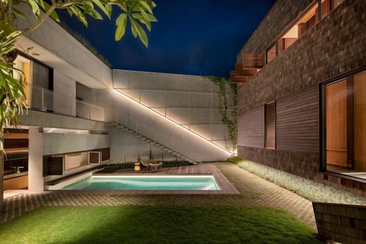 A modern building with a swimming pool, a staircase, and a well-maintained lawn.