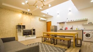 A modern living room with a sofa, a wooden dining table with benches, a TV, and a patterned rug. - Paradise Suite @ Asia City (Kota Kinabalu)