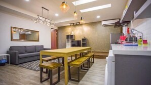 A modern living room with a wooden dining table, grey sofa, and a kitchen area with a fridge and a sink. - Paradise Suite @ Asia City (Kota Kinabalu)