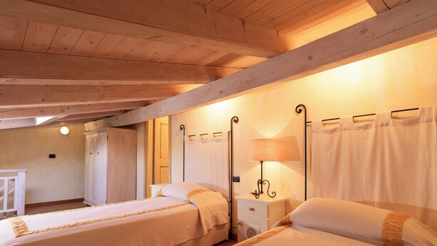 Une chambre avec deux lits, des poutres en bois au plafond, une table de chevet avec une lampe et une armoire.