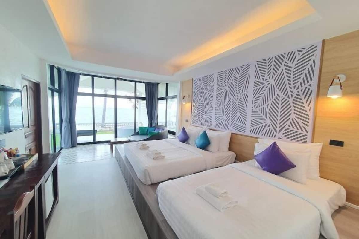 A hotel room with two beds, a TV, a desk, and a large window with curtains.