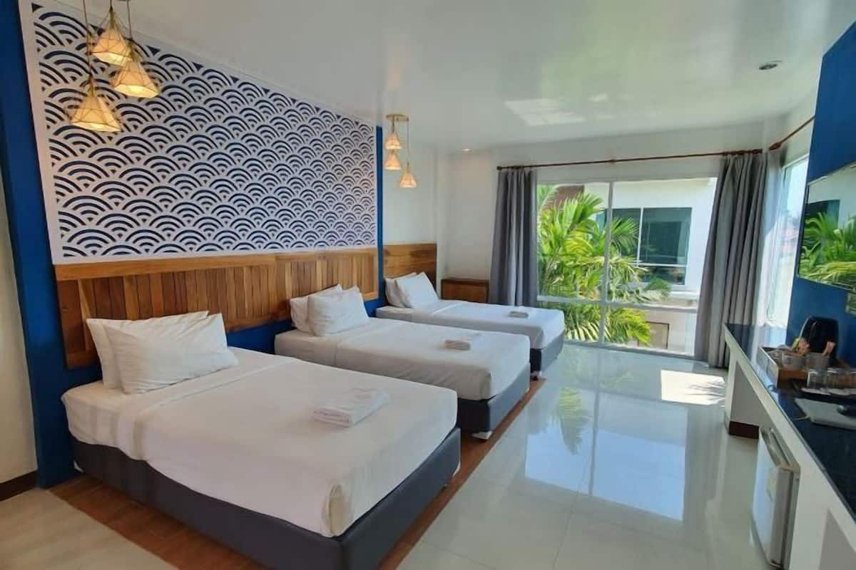 A hotel room with three beds, a wooden headboard, a patterned wall, and a view of greenery outside.