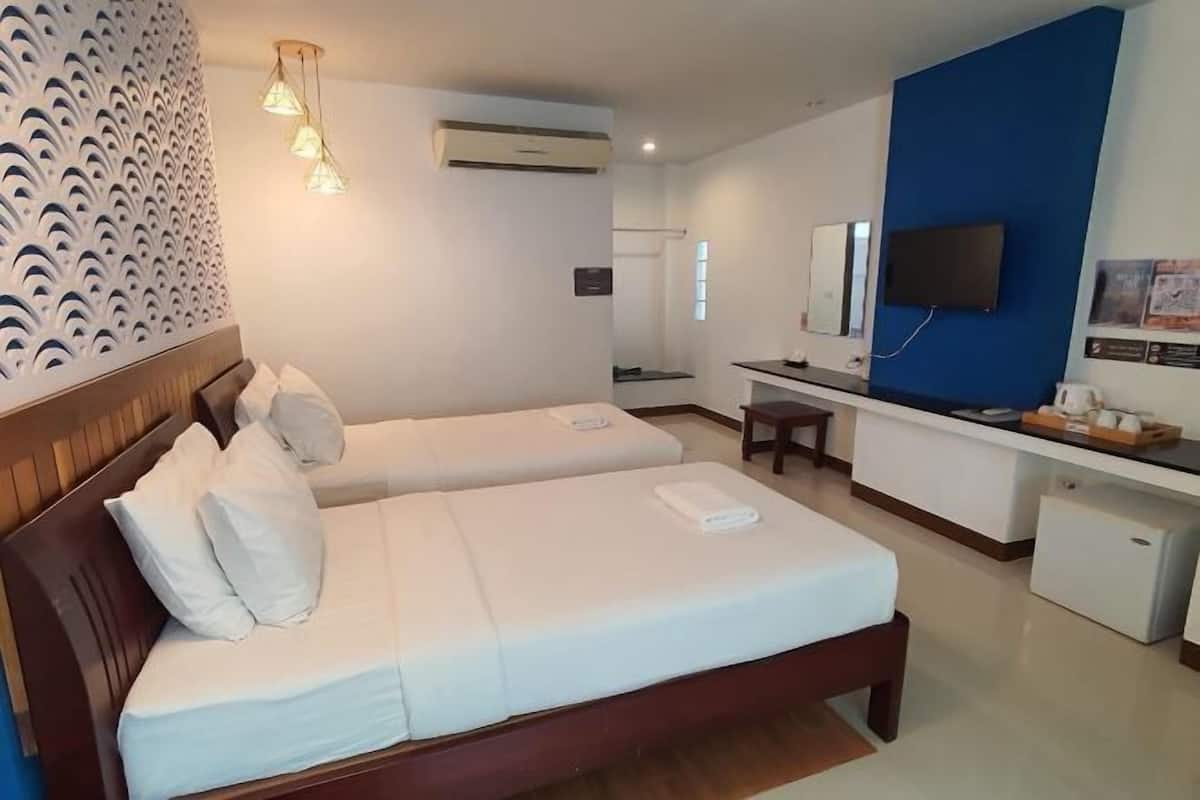 A hotel room with two beds, a desk, a television, and an air conditioning unit.