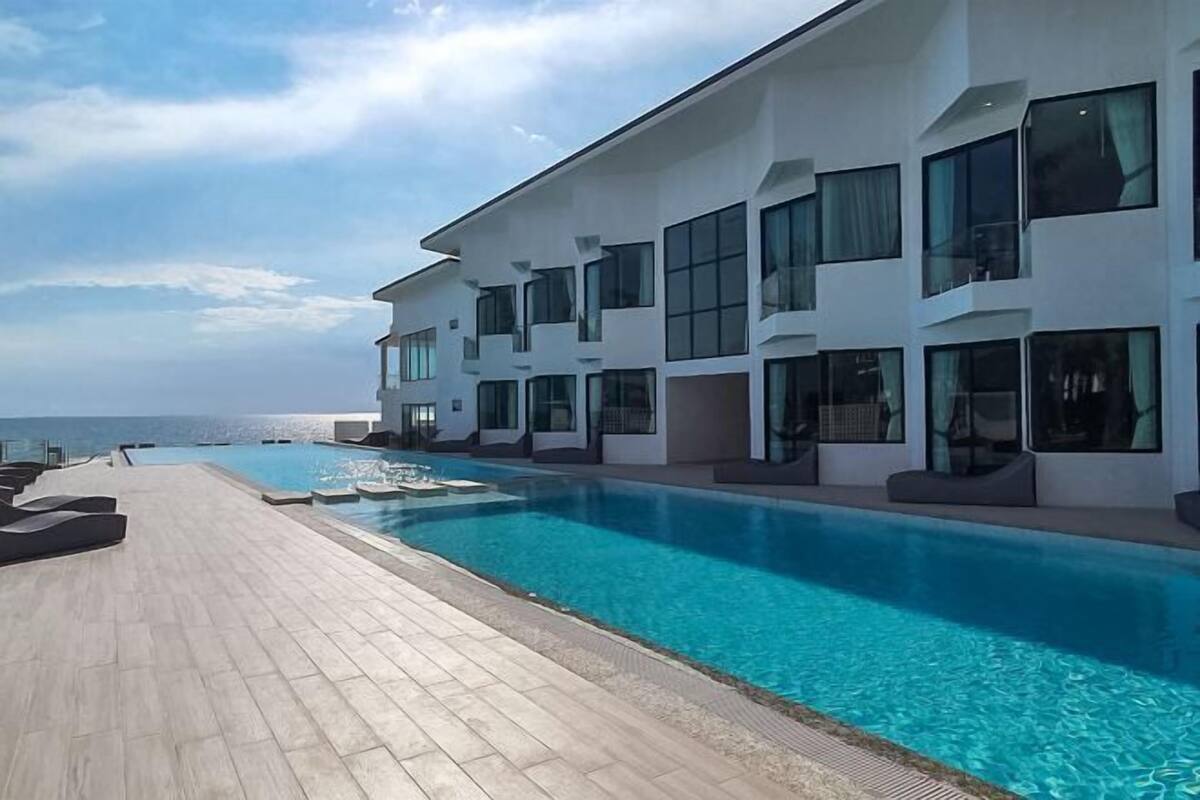 A modern hotel with a swimming pool, large windows, and a view of the sea.
