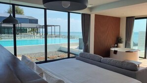 A modern hotel room with a large bed, a seating area, a small table, and a view of an infinity pool. - Rattanapura (Tha Mai)