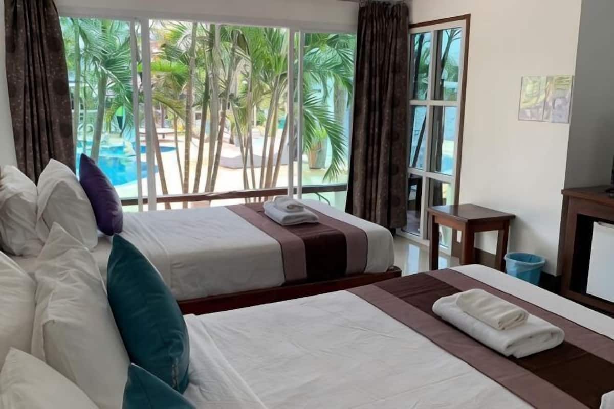 A hotel room with two beds, a view of a pool, and a window with curtains.