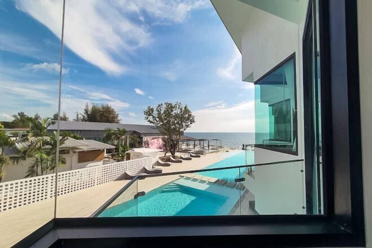 A modern hotel room with a glass balcony overlooking a pool and beach.