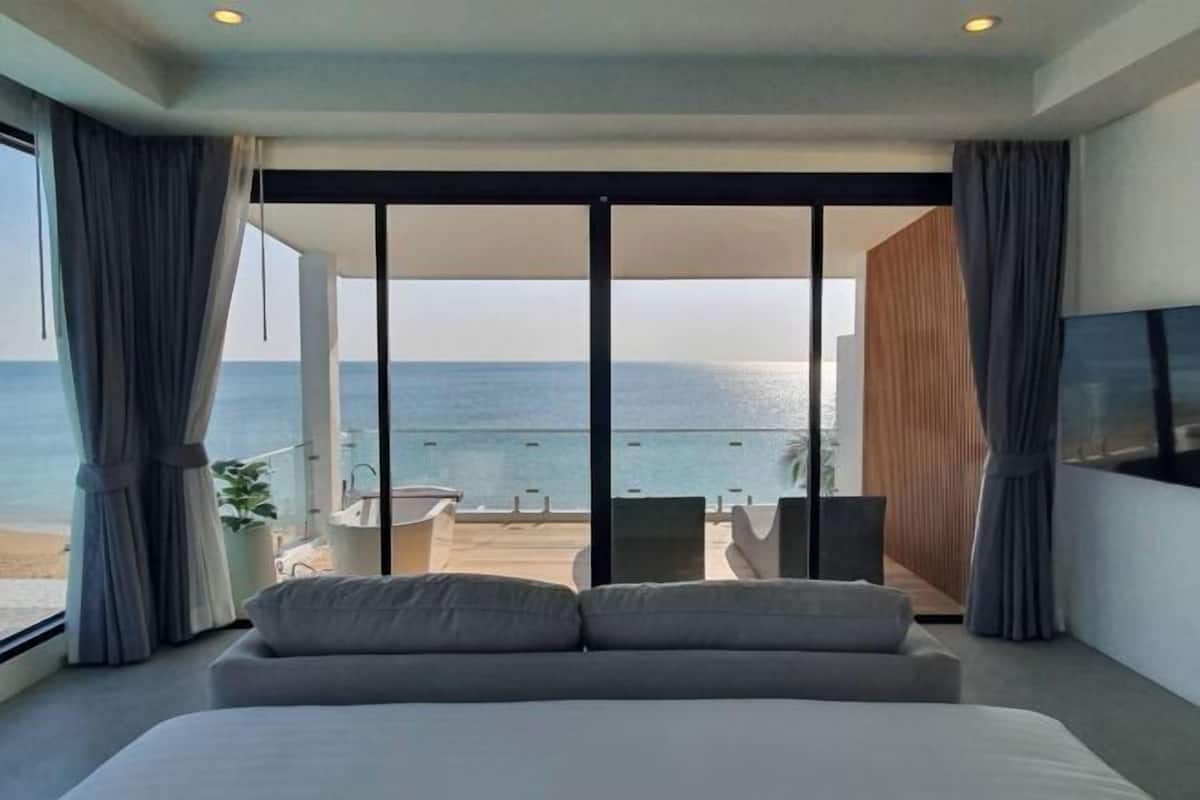 A modern hotel room with a large bed, a TV, and a balcony with a view of the sea.