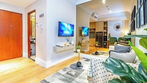 A modern living room with a flat-screen TV, a large mirror, and a wooden floor. - Apartment Roseville SOHO & Suites by Nagisa Bali (Serpong)