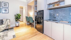 Una cocina moderna con encimera de mármol, horno empotrado y fregadero. Hay una zona de comedor con mesa y sillas, y una planta en la esquina.