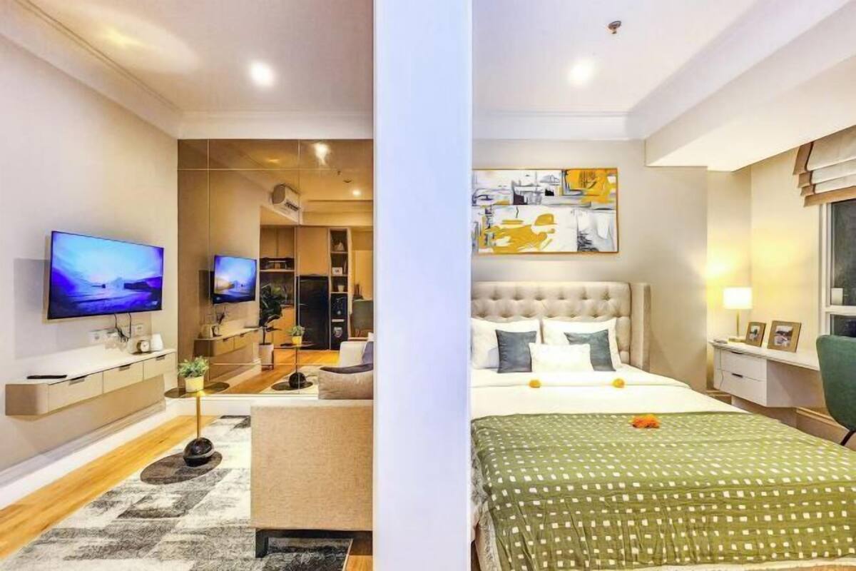 Quarto de hotel moderno com uma cama, televisão, escrivaninha e uma pintura grande na parede.
