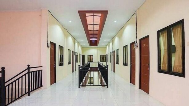 A long, narrow hallway with a central staircase, flanked by doors and windows on both sides. - Urbanview @ Nalaya Homestay Mataram (East Cakranegara)