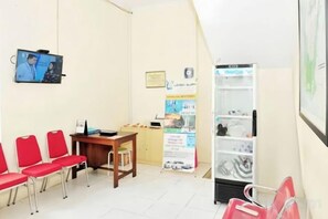 Un área de espera con sillas rojas, una mesa de madera, una pantalla de televisión y un tablón de anuncios.