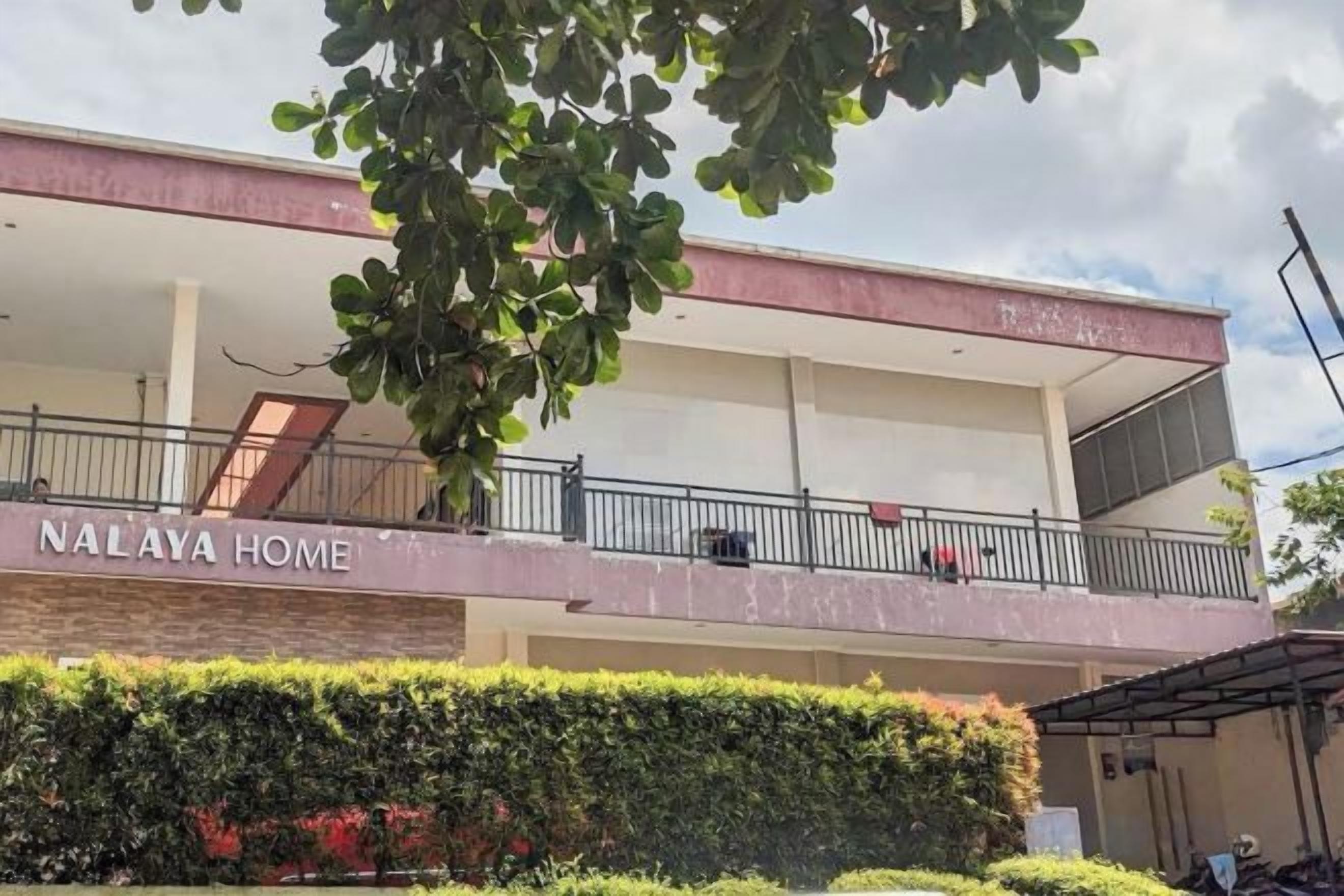 A two-story building with balconies, a sign reading 'NALAYA HOME,' and a well-maintained hedge in the foreground.