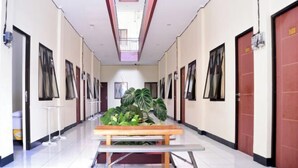 A long, narrow hallway with doors on both sides, a central bench, and a skylight. - Urbanview @ Nalaya Homestay Mataram (East Cakranegara)