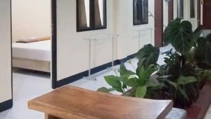 A hotel corridor with a wooden bench, potted plants, and a bed in the background. - Urbanview @ Nalaya Homestay Mataram (East Cakranegara)