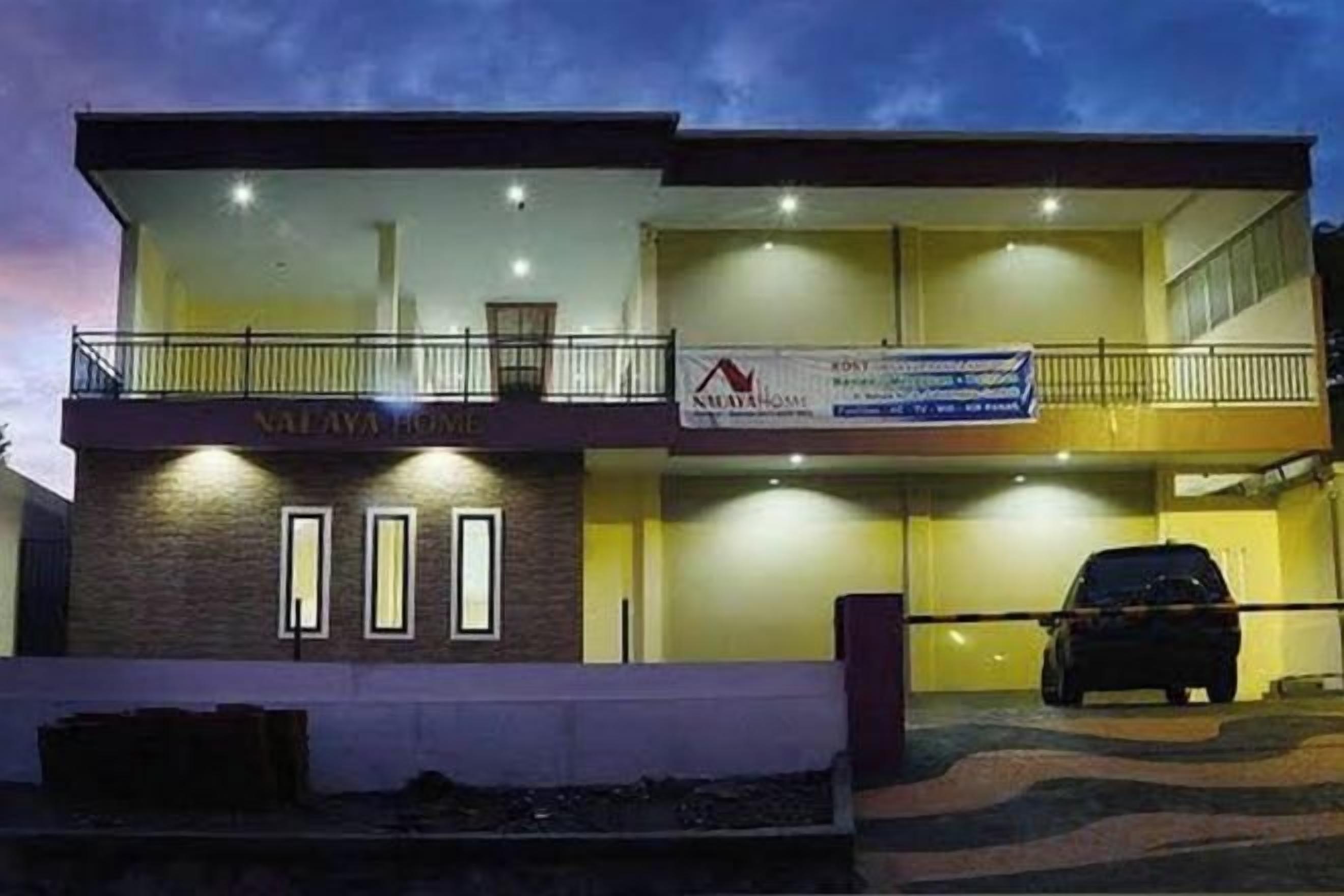 A two-story building with a balcony on the upper level, a car parked in front, and a banner with text.