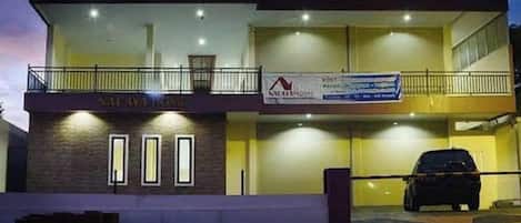 A two-story building with a balcony on the upper level, a car parked in front, and a banner with text.