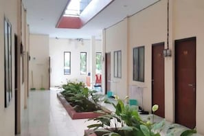A hotel corridor with a row of rooms on the right, a plant bed in the center, and a door with the number 104 on the left. - Urbanview @ Nalaya Homestay Mataram (East Cakranegara)