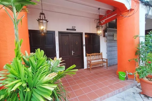 Entrada de hotel con dos puertas, un banco y plantas en macetas.