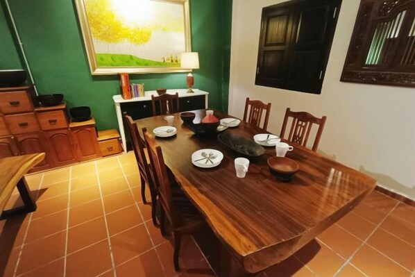 A dining area with a wooden table set for four, surrounded by chairs, with a green wall and a window in the background. - 57 Ruma Oren Heritage Jonker Residence (Melaka)