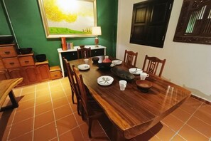 A dining area with a wooden table set for four, surrounded by chairs, with a green wall and a window in the background. - 57 Ruma Oren Heritage Jonker Residence (Melaka)
