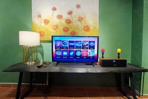 A flat-screen TV on a table with a lamp, a game console, and a painting on the wall. - 57 Ruma Oren Heritage Jonker Residence (Melaka)