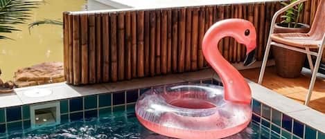 A swimming pool with a pink flamingo float, a wooden deck, and a chair.