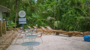 A beachside area with lounge chairs and tables, surrounded by lush greenery. - Phetra Pool Villas (Surat Thani)