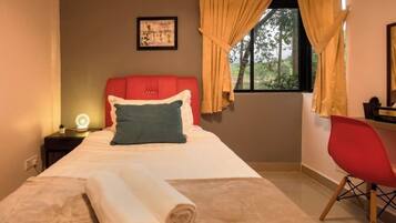 A neatly made bed with a rolled towel, a red headboard, a bedside lamp, and a window with curtains.