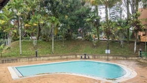 A swimming pool surrounded by palm trees and greenery, with a brick pathway leading to it. - Cozy Genting Permai Resort By THM (Genting Highlands)
