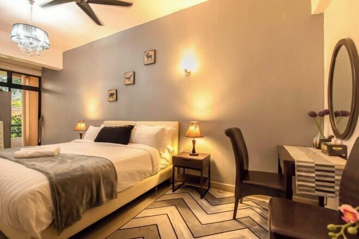 Een slaapkamer met een bed, bedlampen, een bureau, een stoel, een spiegel en wanddecoratie.