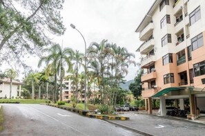 Un immeuble d’habitation doté de nombreux balcons, d’un espace de stationnement couvert et situé dans une rue où sont garées des voitures.
