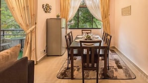 A dining area with a table set for four, a refrigerator, and a view of greenery through the window. - Cozy Genting Permai Resort By THM (Genting Highlands)
