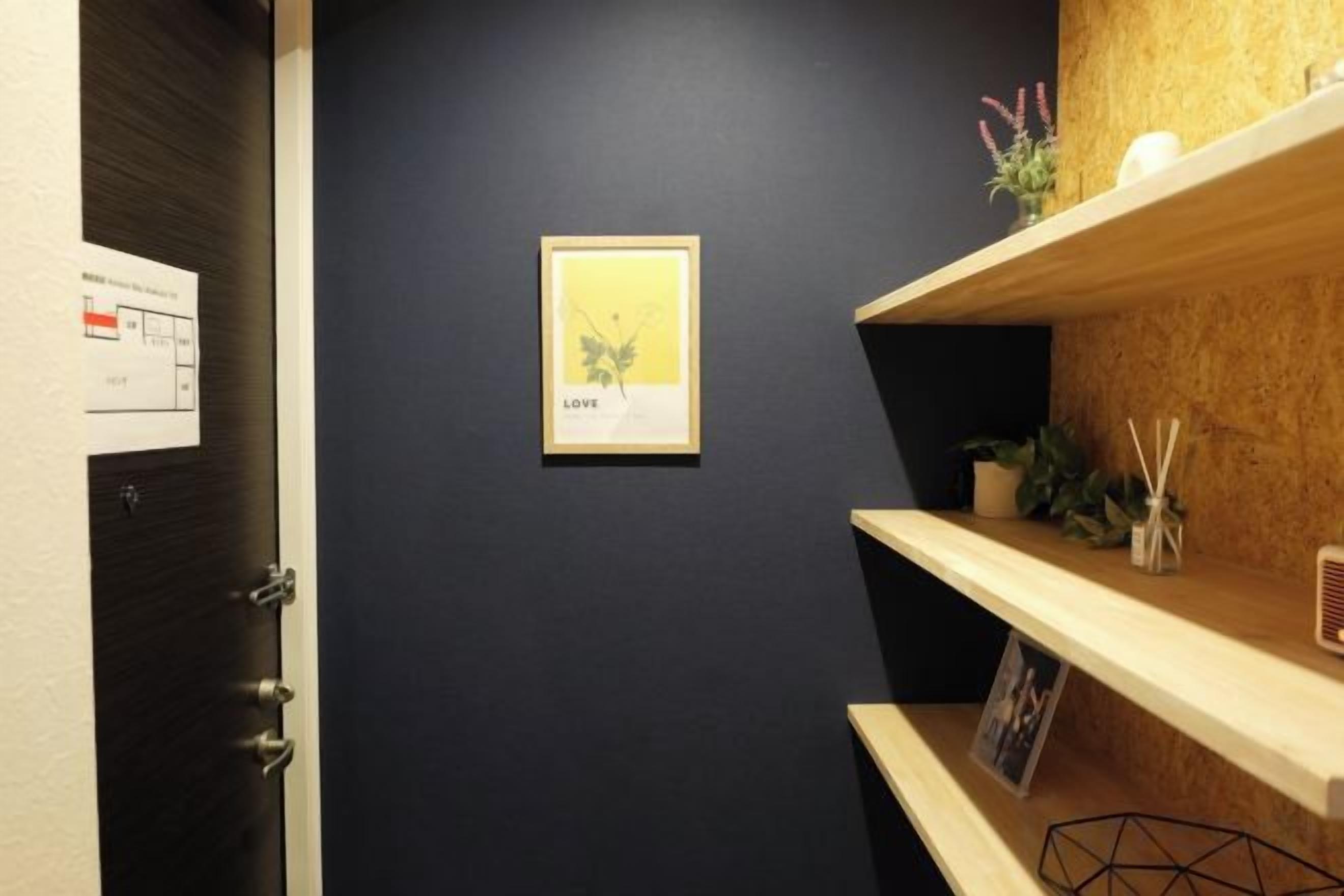 A hallway with a dark wall, a framed picture with the word 'LOVE,' and wooden shelves with plants and a small table.