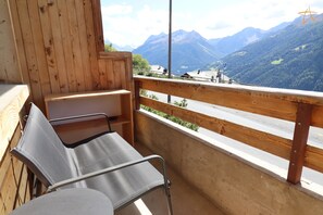 A balcony with a view of mountains, a wooden wall, and a metal chair.