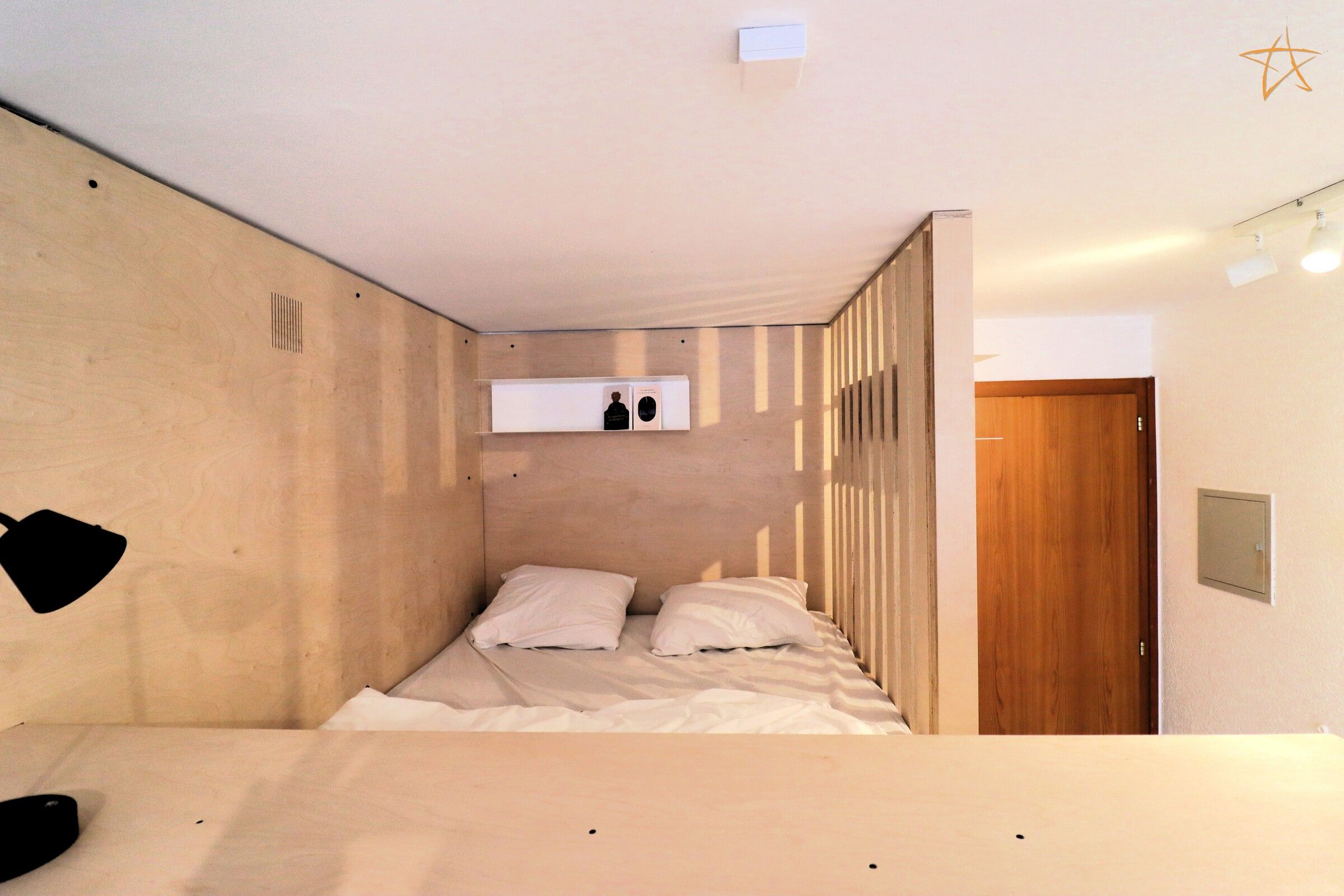 A room with a bed, a wooden door, and a wall-mounted shelf with items.