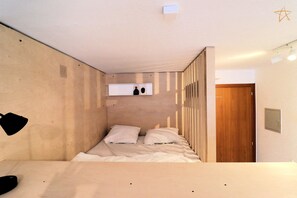 Una habitación con una cama, una puerta de madera y un estante en la pared con objetos.