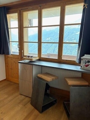 A kitchen with a window, wooden counter, and stools.