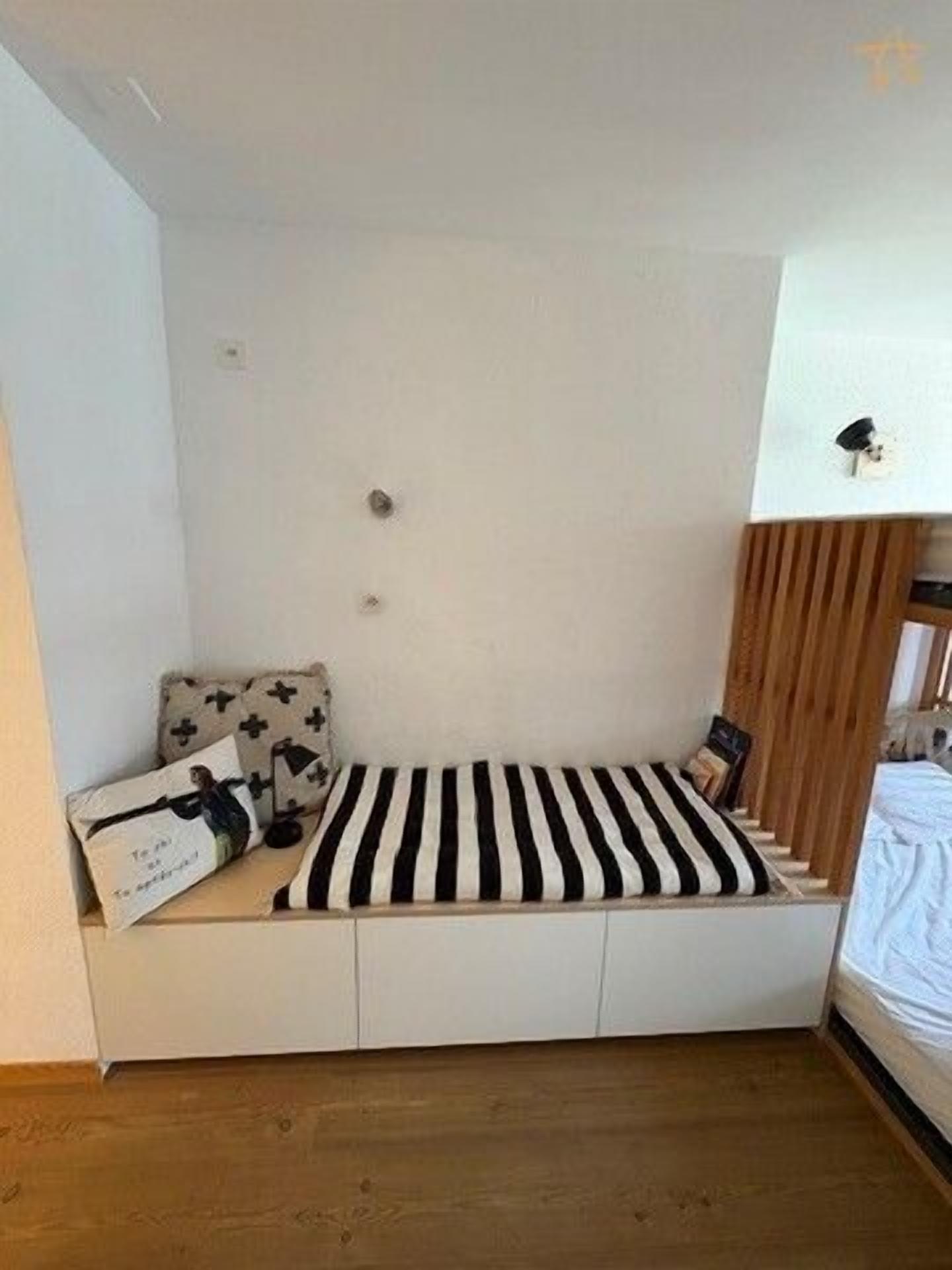 A room with a built-in bed, a wooden slat bench, and a small table with a pillow.