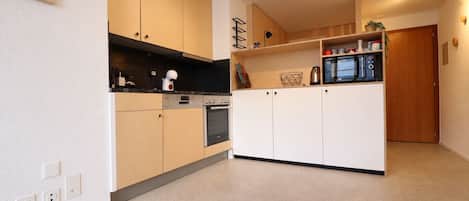 A modern kitchen with light wood cabinets, a black countertop, and a built-in microwave.