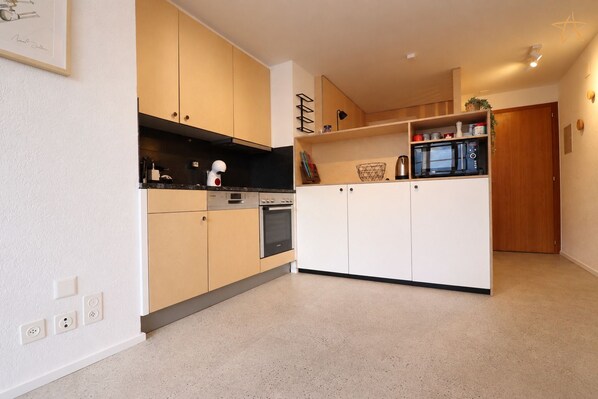 A modern kitchen with light wood cabinets, a black countertop, and a built-in microwave.