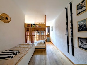 A narrow room with a bed, a wooden partition, and skis on the wall.