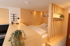 A modern bedroom with a bed, bedside table, lamp, and a plant.