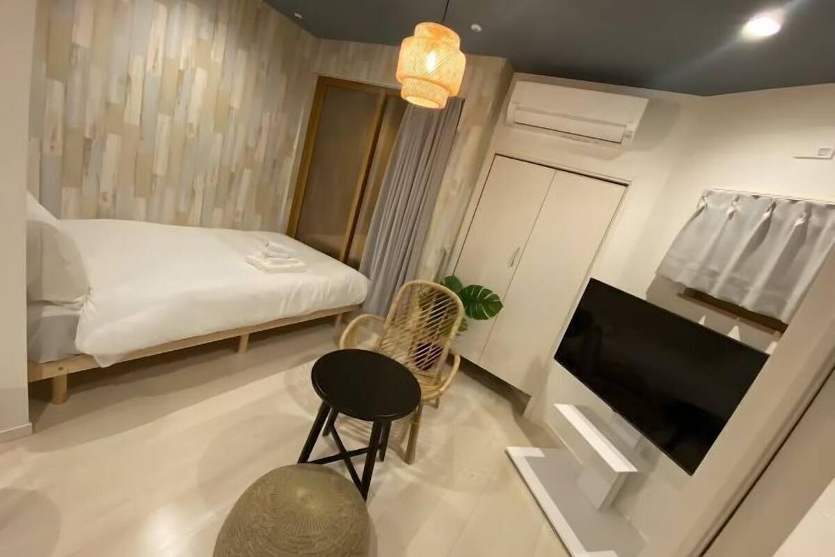 A modern hotel room with a bed, a TV, a wardrobe, and a small seating area.