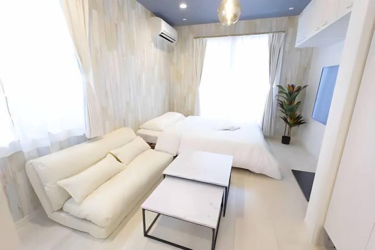 A modern hotel room with a sofa, a bed, a small table, and a potted plant.